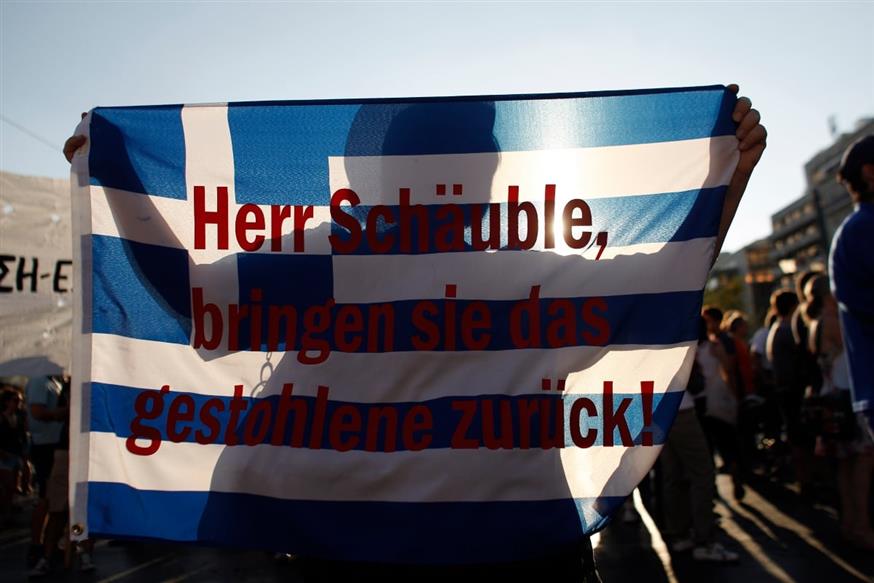 Διαδηλωτής κρατά ελληνική σημαία με ένα σύνθημα που γράφει «Κύριε Σόιμπλε φέρτε πίσω τα κλεμμένα»./ copyright Ap Photos