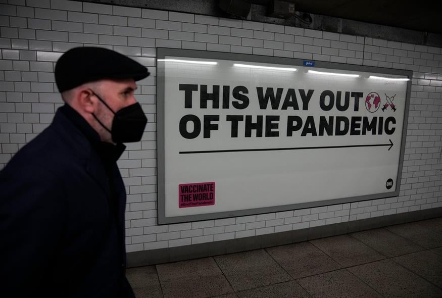 Άνδρας που φοράει μάσκα προσώπου για να περιορίσει την εξάπλωση του κορονοϊού περπατά μπροστά από μια αφίσα εκστρατείας για την υγεία / AP Photo/Matt Dunham