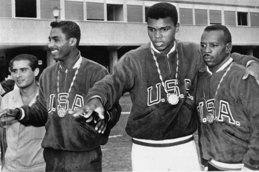 Ο Κάσιους Κλέι με το χρυσό ολυμπιακό μετάλλιο στο στήθος. Αριστερά του ο Γουίλμπερτ ΜακΚλουρ και δεξιά του ο Έντουαρντ Κρουκ, επίσης χρυσοί Ολυμπιονίκες.