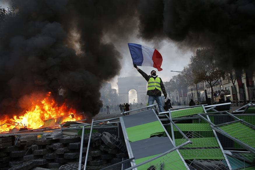 Διαδηλωτής με κίτρινο γιλέκο και γαλλική σημαία, στο κέντρο του Παρισιού (AP Photo/Michel Euler)