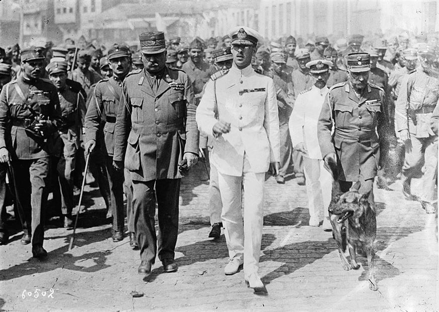 Ο βασιλιάς Αλέξανδρος στη μέση με τη λευκή στολή. Το μοιραίο σκυλί του ο Φριτς δεξιά. Αριστερά εικονίζεται ο στρατηγός Λεωνίδας Παρασκευόπουλος. / copyright wikimedia.org