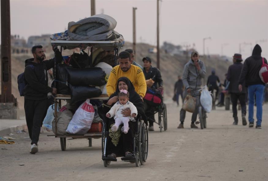 Ένας εκτοπισμένος Παλαιστίνιος σπρώχνει μια γυναίκα σε αναπηρικό καροτσάκι που κρατά ένα μωρό σε δρόμο για να επιστρέψουν στα σπίτια τους στη βόρεια Λωρίδα της Γάζας/AP Photos