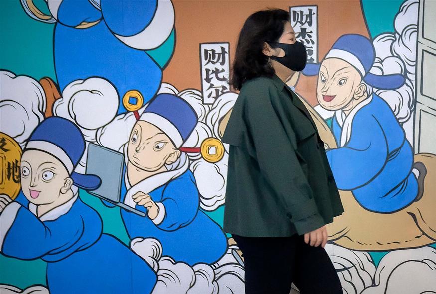 Μια γυναίκα με μάσκα προσώπου περπατά μπροστά από μια τοιχογραφία στο Πεκίνο  (AP Photo/Mark Schiefelbein)