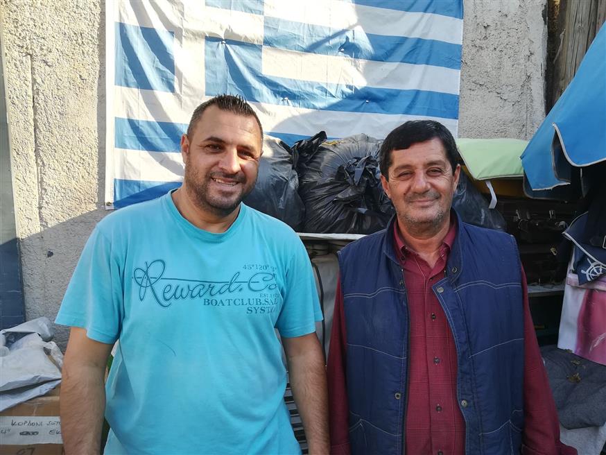 O Ερτσάν Χασάν και ο μπαμπάς του Ραΐφ Χασάν μπροστά από την ελληνική σημαία στο παζάρι της «Προόδου»
