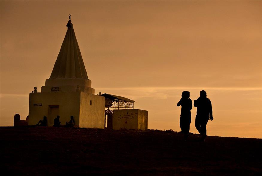 Ο ήλιος δύει καθώς οι γυναίκες επισκέπτονται ένα ιερό των Γιαζίντι με θέα στον καταυλισμό Kankhe για τους εσωτερικά εκτοπισμένους στο Dahuk, στο βόρειο Ιράκ / AP Photo/Maya Alleruzzo