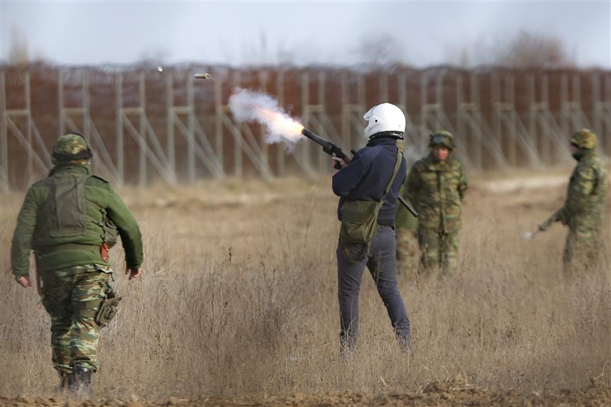 Αστυνομικοί πετούν χημικά προς την πλευρά προσφύγων και μεταναστών (AP Photo/Giannis Papanikos)