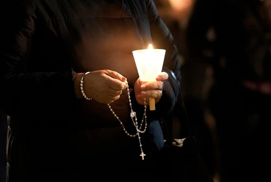 Μια γυναίκα κρατά ένα ροζάριο και ένα κερί σε εκκλησία  (AP Photo/Armando Franca)