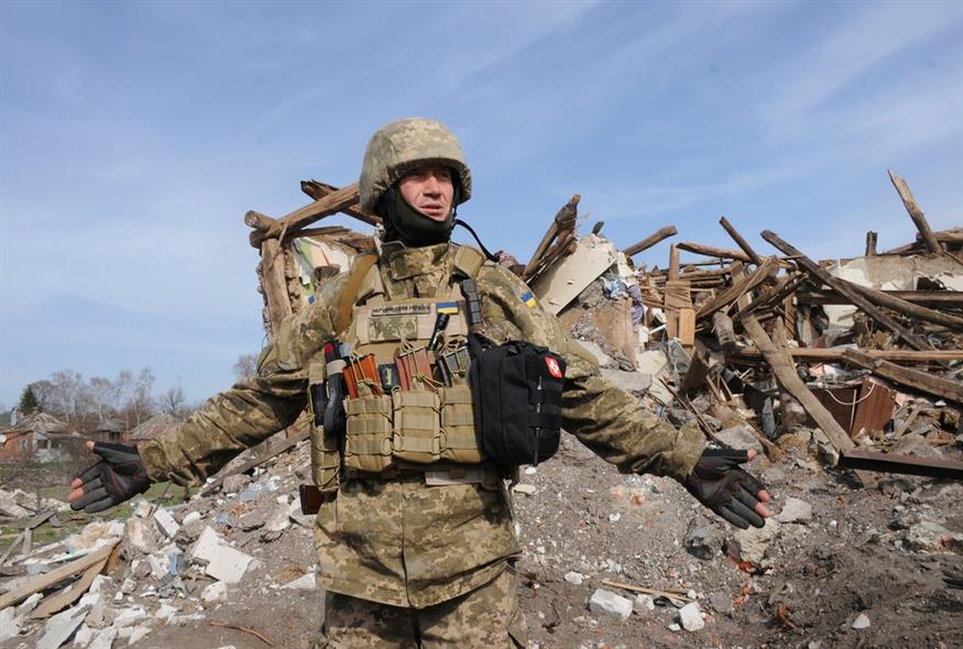 Ουκρανός στρατιώτης ανοίγει τα χέρια του μπροστά από πολυκατοικία που υπέστη ζημιές από βομβαρδισμό στην πόλη Chuhuiv, περιοχή Χάρκοβο / AP Photo/Andrew Marienko