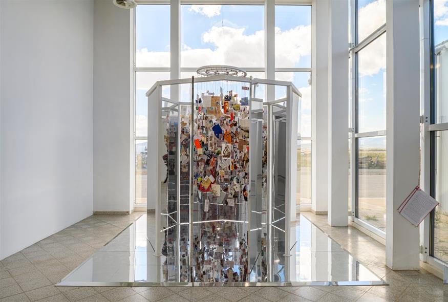 Λίνα Πηγαδιώτη, …μετάβαση…, «Το συγκεκριμένο έργο αξιοποιεί το φυσικό φως — το μόνο σημείο σε ολόκληρο τον χώρο απ’ όπου υπάρχει οπτική επαφή με τον αεροδιάδρομο προσγείωσης και απογείωσης» περιγράφει ο κ. Πράπογλου. «Πρόκειται για μια εγκατάσταση φτιαγμένη από καθρέφτες. Ο επισκέπτης μπορεί να μπει μέσα και να δει το φως να θρυμματίζεται, ενώ η δική του αντανάκλαση μπερδεύεται με τα προσωπικά αντικείμενα της καλλιτέχνιδας. Είμαι βέβαιος πως ο καθένας θα αναγνωρίσει κάτι δικό του ανάμεσα σε αυτά» προσθέτει (Copyright: Christos Simatos)