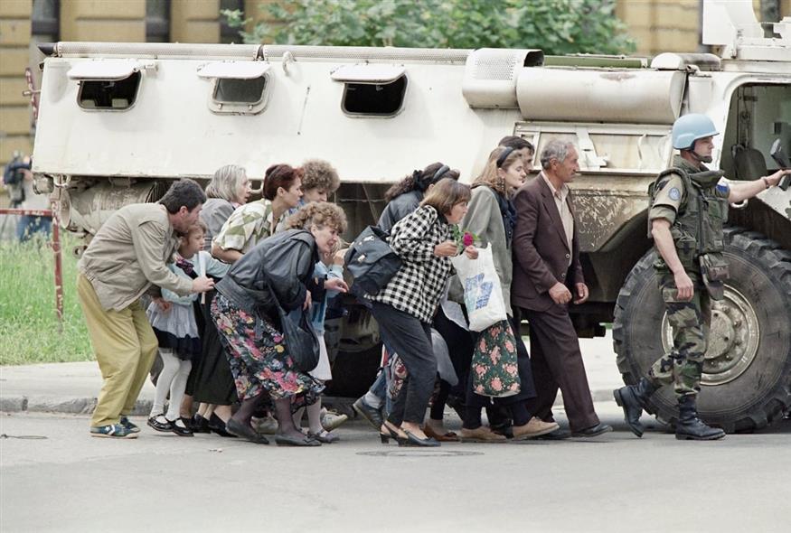 Βόσνιοι άμαχοι κάτοικοι του Σαράγεβο προφυλάσσονται πίσω από ένα θωρακισμένο όχημα των κυανόκρανων του ΟΗΕ από τα πυρά ενός Σέρβου ελεύθερου σκοπευτή, στο κέντρο της πόλης το 1995 (David Brauchli/AP)